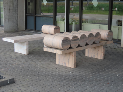 915020 Afbeelding van een kunstwerk bestaande uit twee marmeren banken met daarop marmeren rollen, bij de ingang van de ...